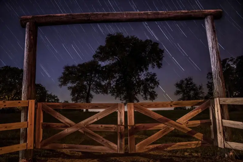 A ranch gate and split-rail fence under the night sky
