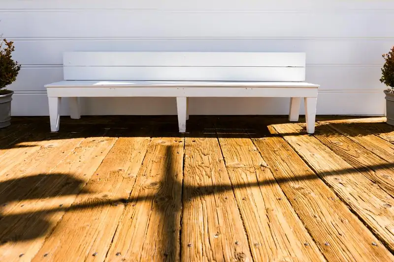 A white bench on a sunlit wooden deck